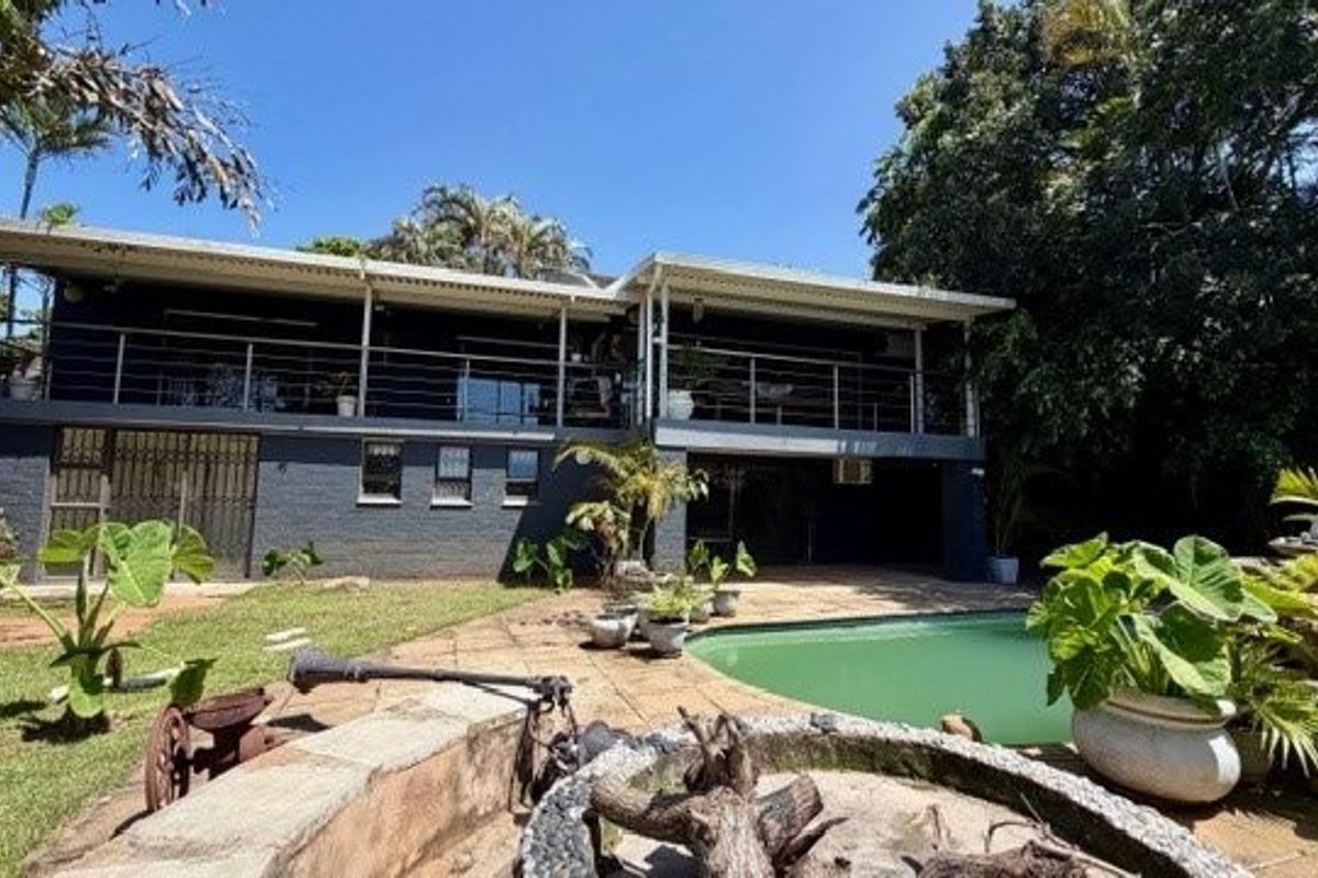Rear view of the property featuring a swimming pool, stone patio, and a spacious elevated balcony overlooking the garden.