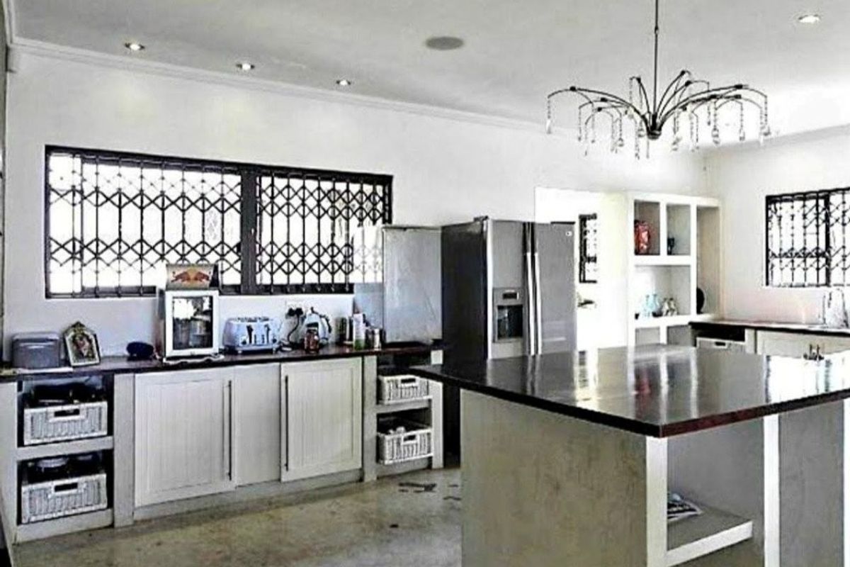 A spacious kitchen featuring a large central island, built-in cabinetry, and security bars on the windows, offering a functional layout with potential for modernization.