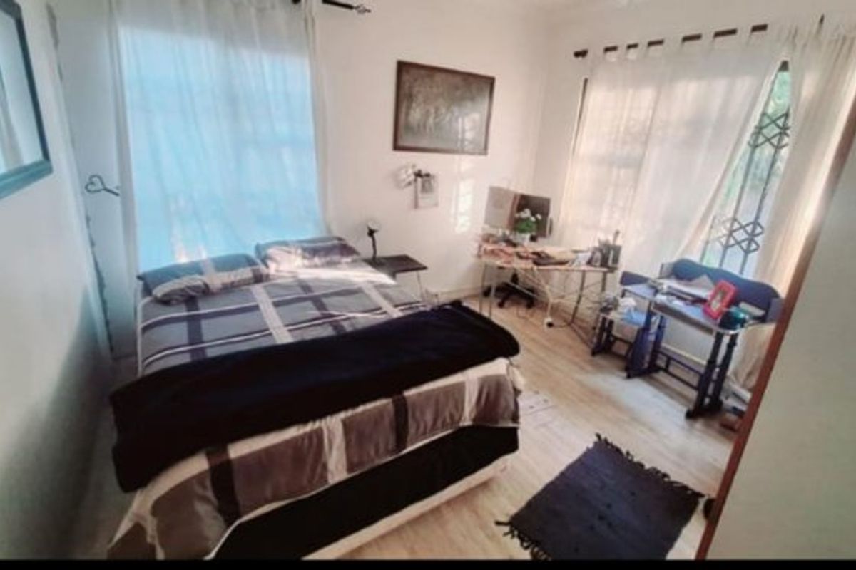 A bedroom featuring laminate flooring and large windows with security gates, providing natural light.