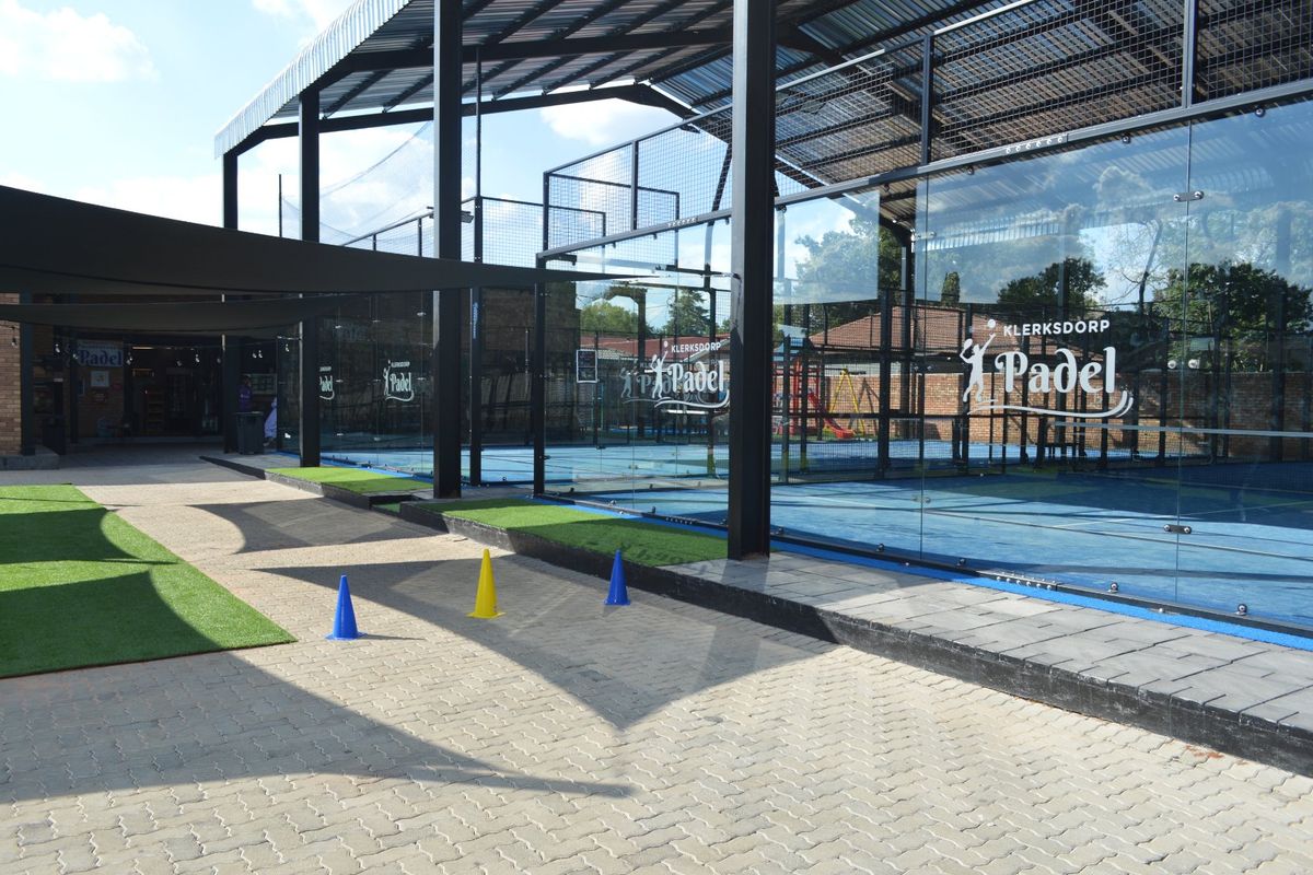 Modern outdoor padel court facility featuring professional glass enclosures, steel structural roofing, and well-maintained paved surroundings.