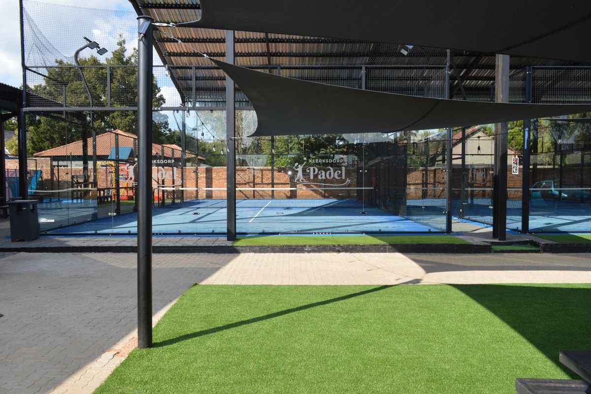 A well-maintained outdoor padel court facility featuring professional glass and mesh enclosures, artificial turf surfacing, and overhead shade structures.