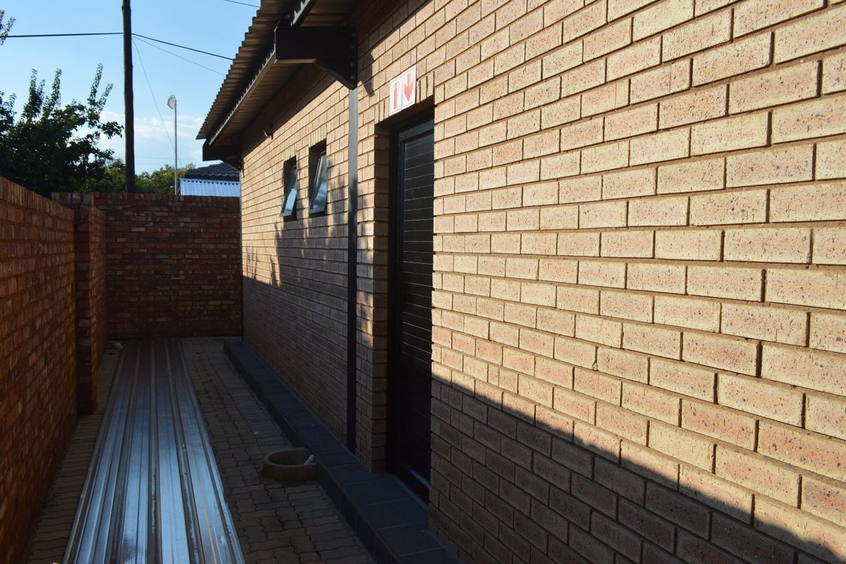 A side view of a commercial building featuring face brick walls, a paved walkway, and a secure entrance door.