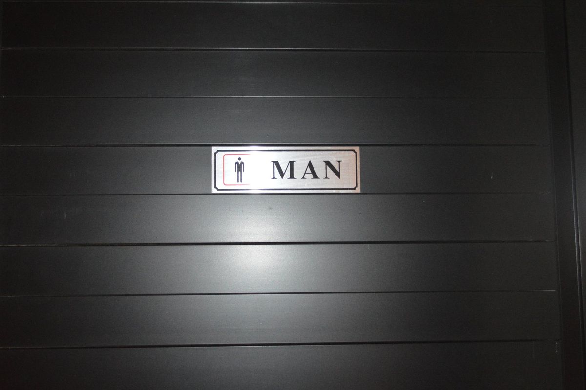 A close-up view of a men's restroom door featuring a clear, modern identification sign.