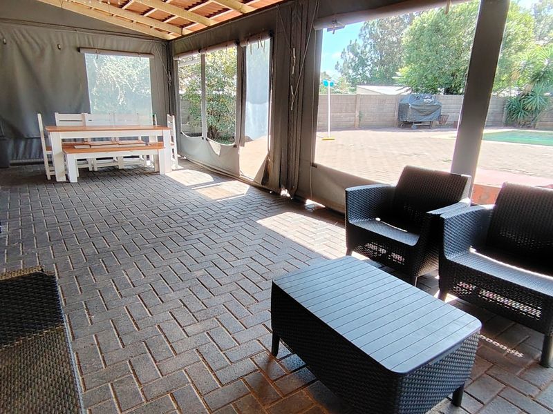 Covered outdoor patio area featuring paved flooring, exposed timber rafters, and retractable canvas blinds, overlooking a private garden and swimming pool.