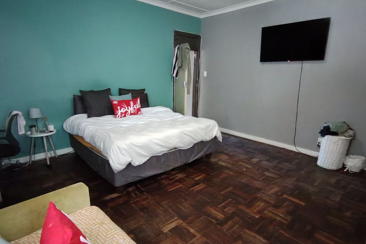 Spacious bedroom featuring classic parquet flooring and a dual-tone wall finish, offering a functional layout with ample space for bedroom furniture.
