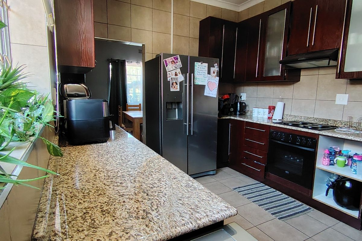 A functional kitchen featuring dark wood cabinetry, granite countertops, a built-in oven, and a hob, with tiled walls and flooring throughout.