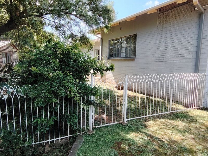 Rear exterior view of the property featuring painted brick walls, steel window frames, and a metal security fence enclosing the garden area.