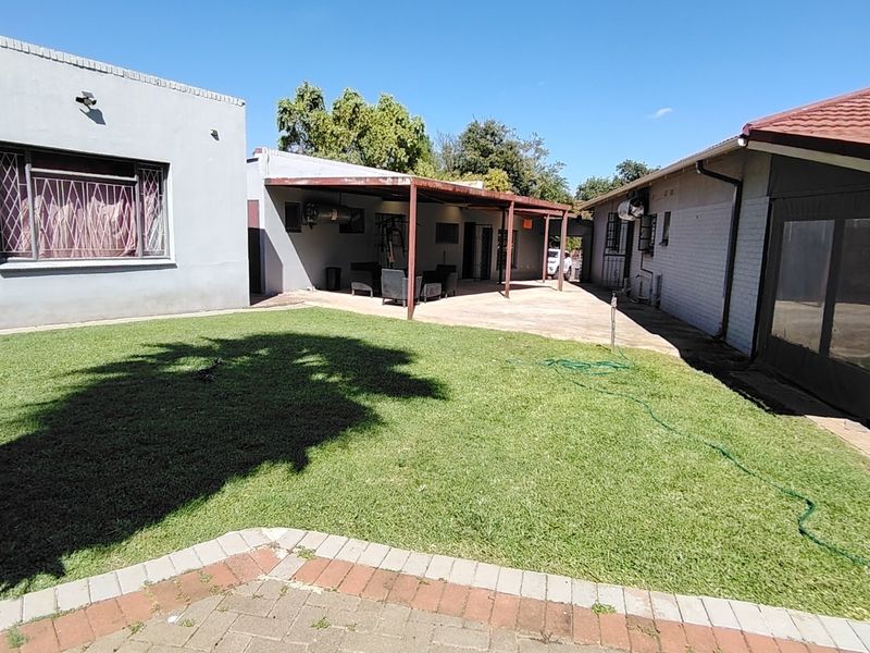 A rear garden view featuring a lawn, a paved walkway, and a covered patio area attached to the main house structure.