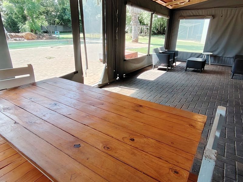 Covered outdoor patio area featuring paved flooring, timber roof structure, and roll-up canvas blinds, overlooking the garden and swimming pool.