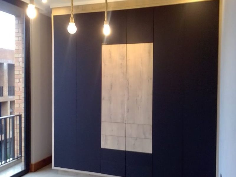 Modern bedroom featuring sleek built-in cupboards with contrasting wood-look panels, tiled flooring, and access to a private balcony.