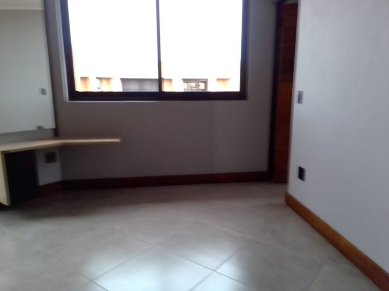 An empty bedroom featuring tiled flooring, timber skirting boards, a built-in desk, and a large sliding window providing natural light.