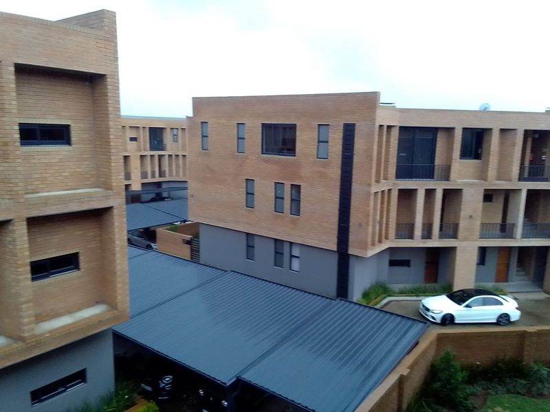 An elevated view of a modern apartment complex featuring face brick architecture, metal roof carports, and private balconies.