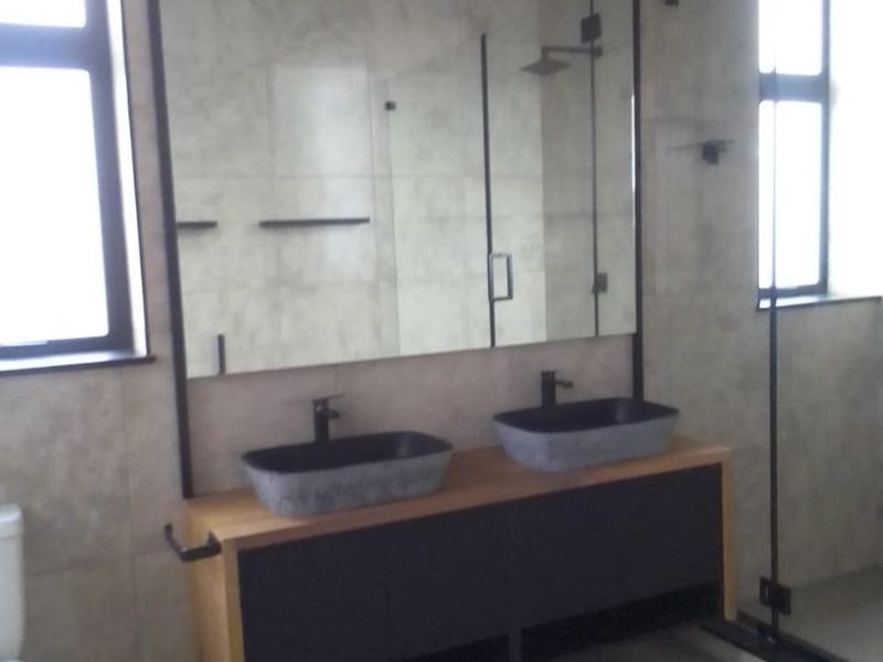 Modern bathroom featuring a double vanity with vessel sinks, large wall-mounted mirror, and a spacious walk-in shower with glass enclosure.