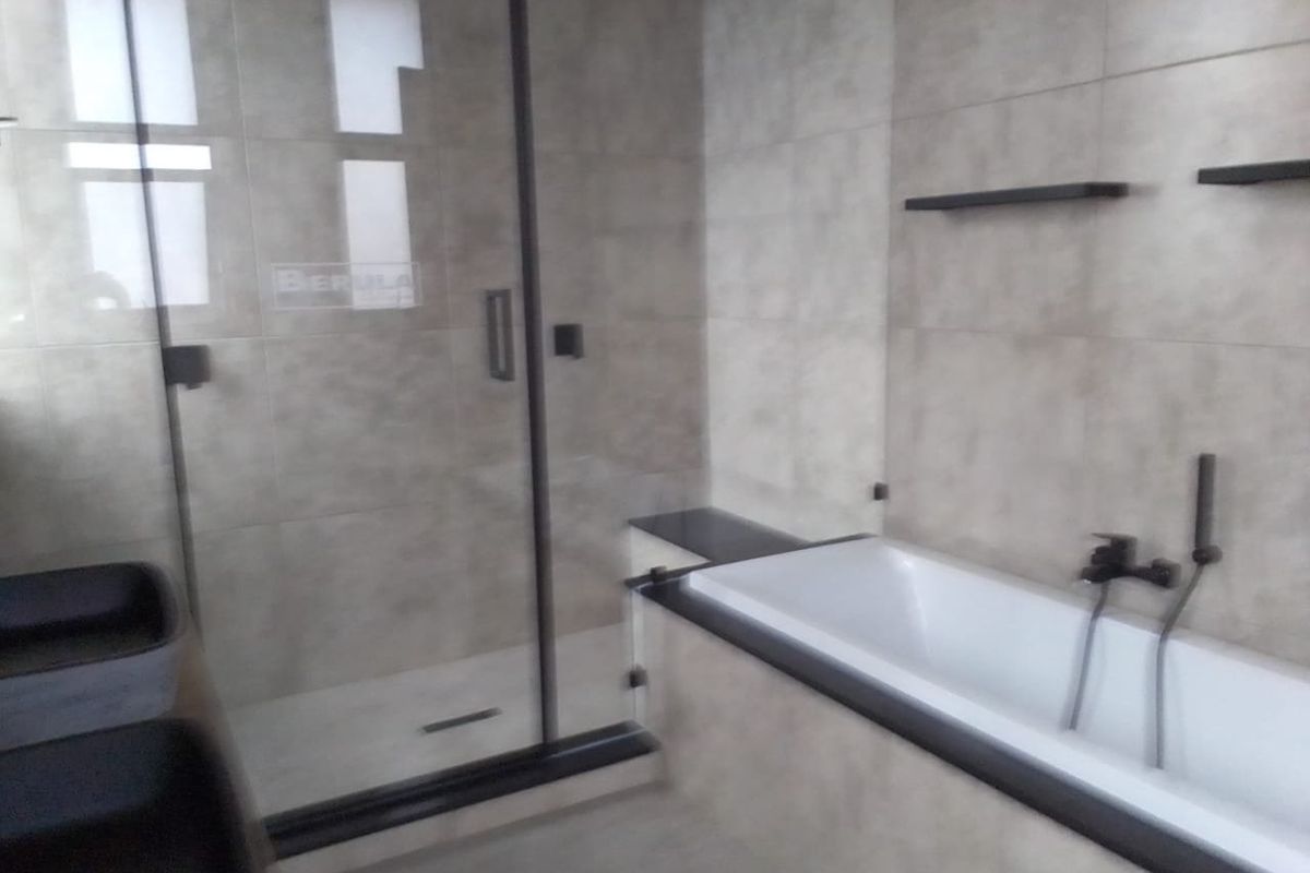 Modern bathroom featuring a glass-enclosed shower, a built-in bathtub with matte black fixtures, and neutral wall tiling.