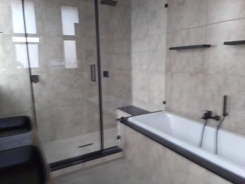 Modern bathroom featuring a glass-enclosed shower, a built-in bathtub with matte black fixtures, and neutral wall tiling.