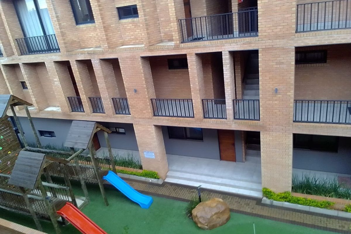 Exterior view of an apartment complex featuring face brick architecture, private balconies, and a communal ground-level play area with artificial turf.