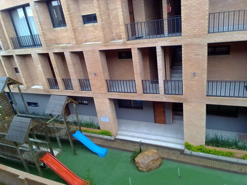 Exterior view of an apartment complex featuring face brick architecture, private balconies, and a communal ground-level play area with artificial turf.