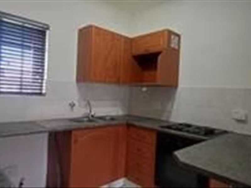 A functional kitchen featuring wooden cabinetry, laminate countertops, a built-in oven with gas hob, and a tiled splashback.