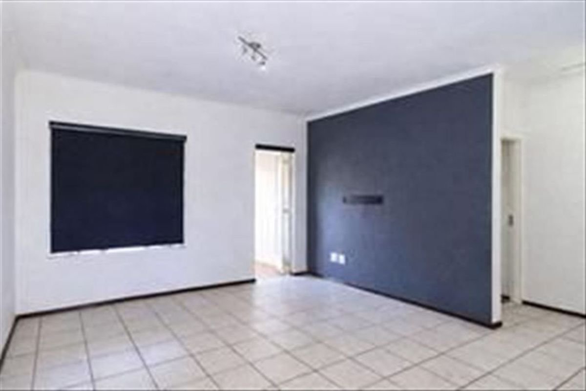 An empty living room featuring tiled flooring, a dark accent wall, and a window fitted with a roller blind.