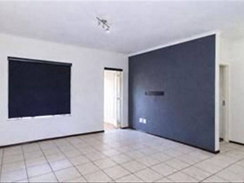 An empty living room featuring tiled flooring, a dark accent wall, and a window fitted with a roller blind.