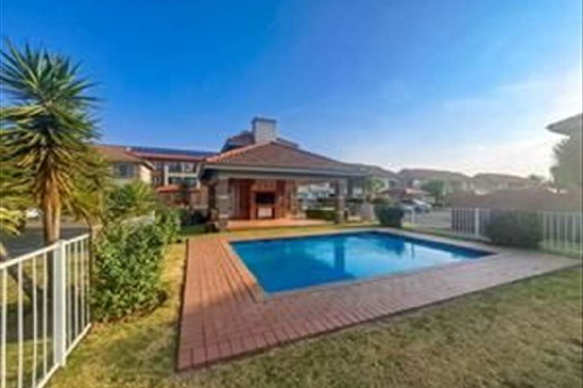 Outdoor pool area featuring a swimming pool, brick paved surround, and a covered patio with a built-in braai facility.
