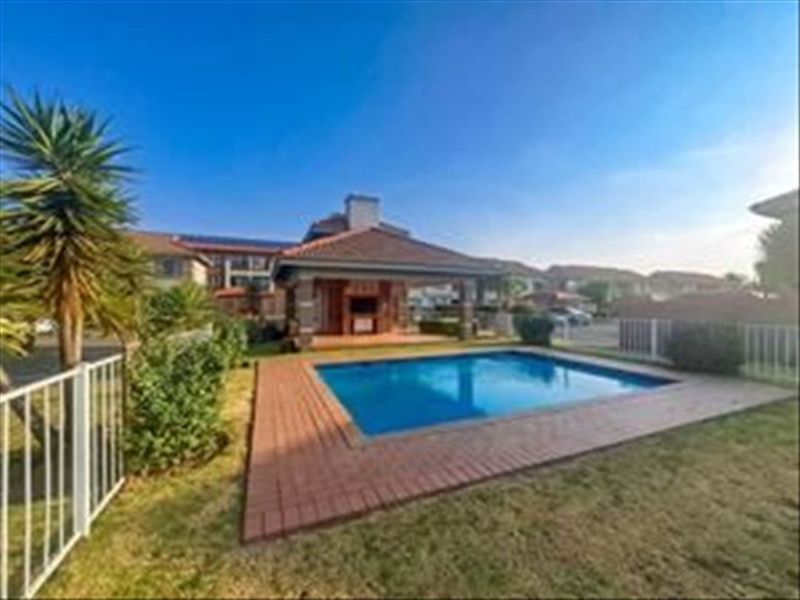 Outdoor pool area featuring a swimming pool, brick paved surround, and a covered patio with a built-in braai facility.