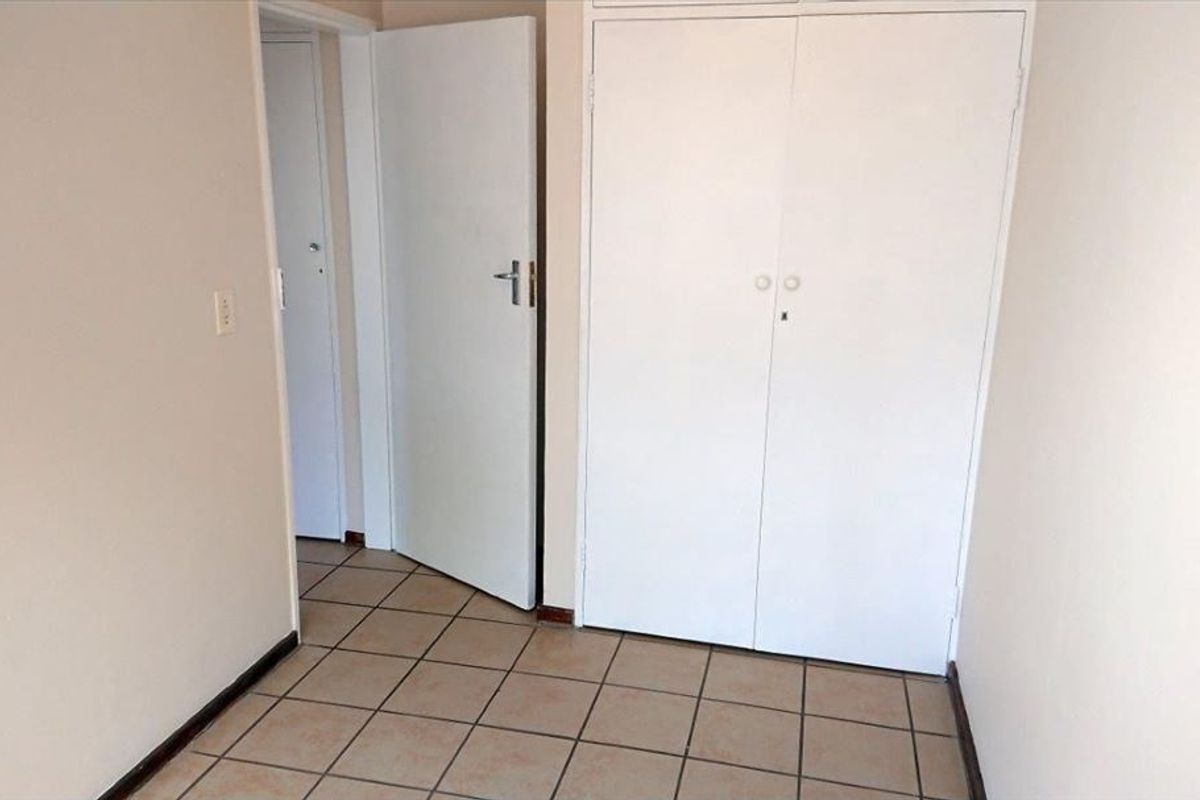 An empty bedroom featuring tiled flooring and built-in cupboards, providing a neutral space ready for personalization.