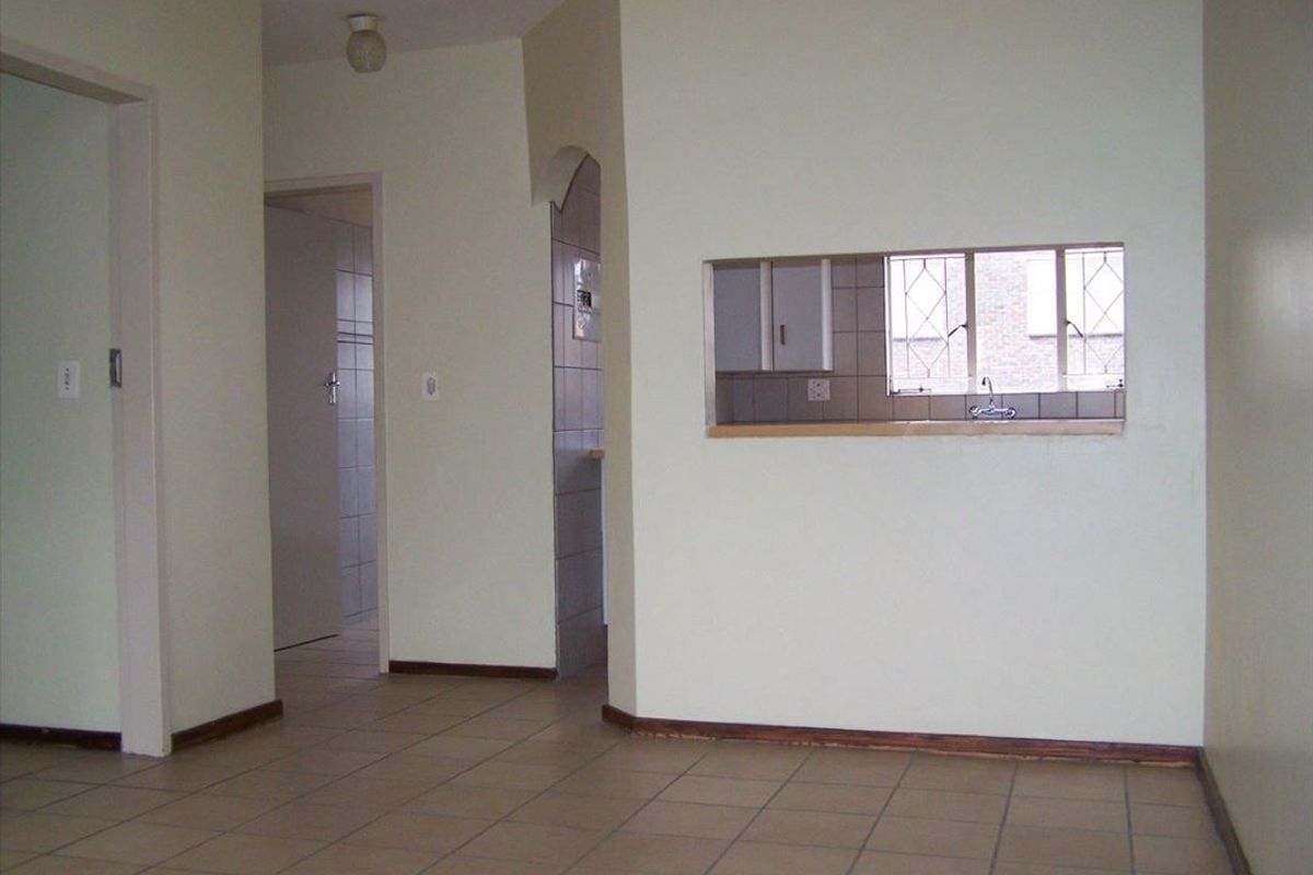 An empty living area featuring tiled flooring and a convenient serving hatch connecting to the kitchen space.