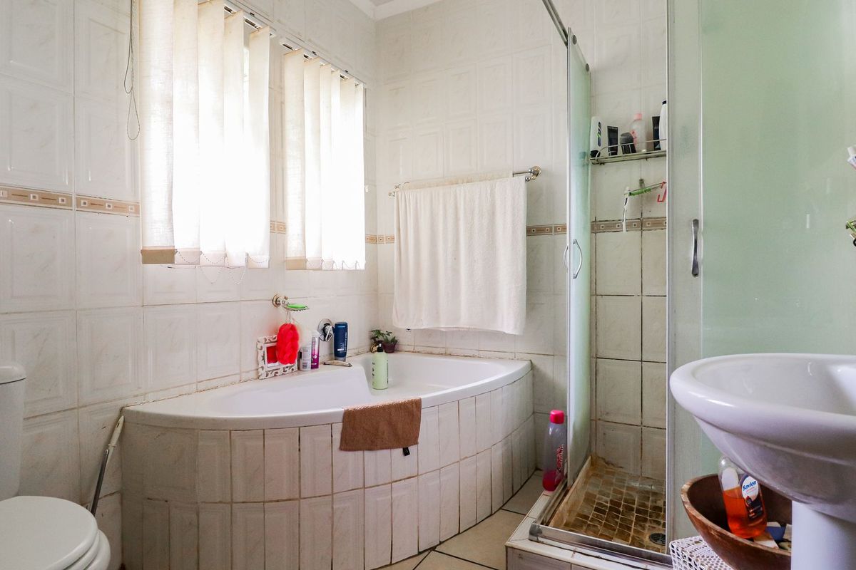 A functional bathroom featuring a built-in bathtub, separate shower enclosure, pedestal sink, and toilet with tiled finishes throughout.