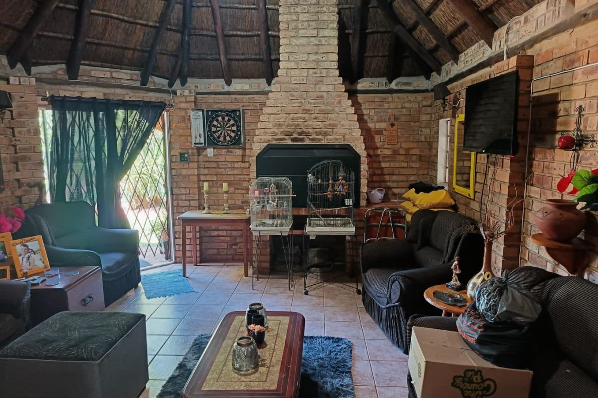 Rustic living room featuring a traditional thatched roof, exposed brick walls, and a central built-in fireplace with tiled flooring throughout.