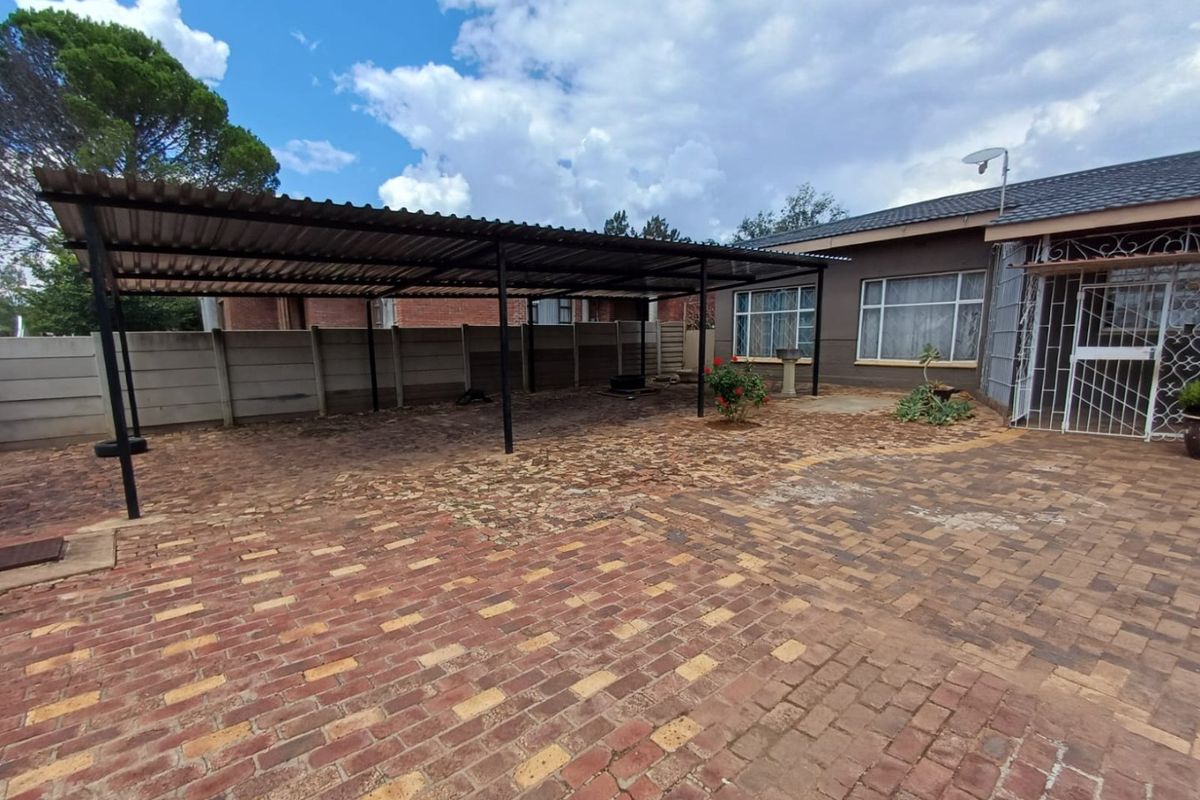 Rear exterior area featuring a large metal carport, extensive brick paving, and secure perimeter walling.