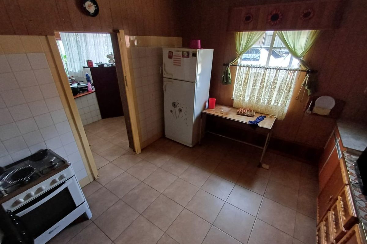 A dated kitchen featuring tiled flooring, wood-paneled walls, and a gas stove, with an adjacent scullery or utility area visible through the doorway.