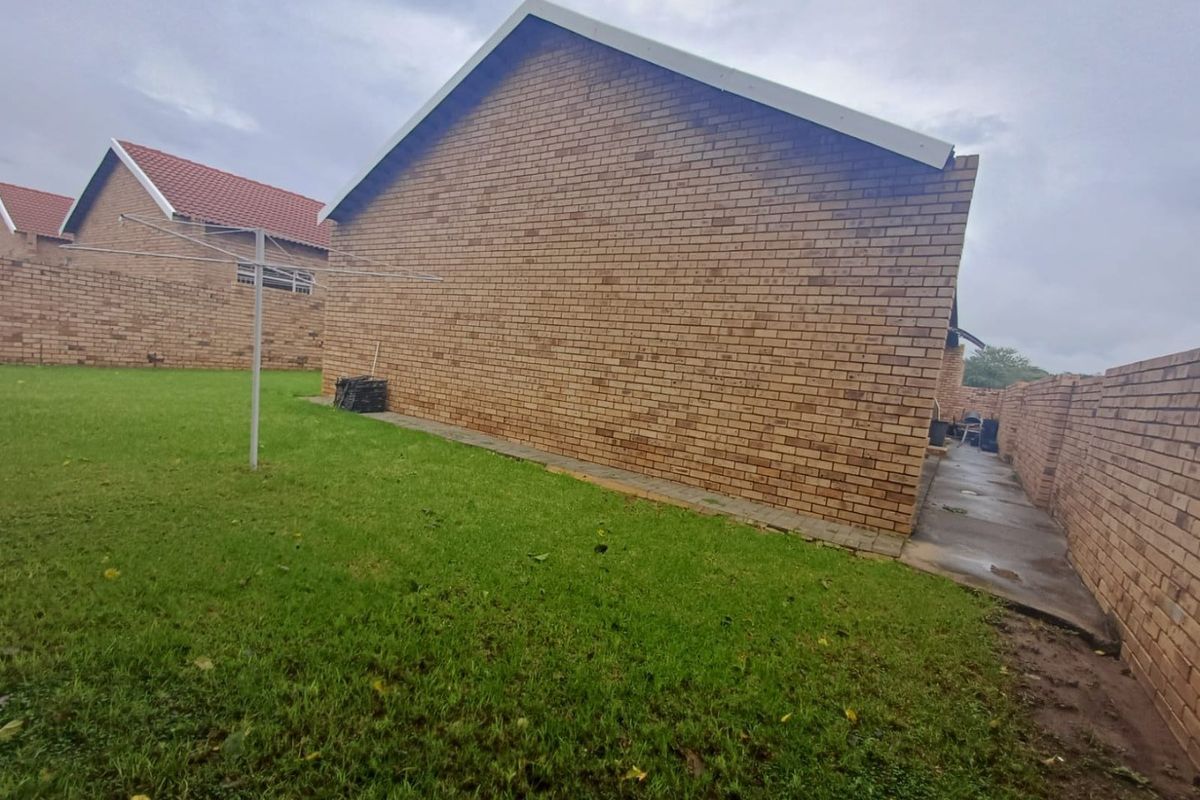 A view of the side and rear exterior of the townhouse, featuring face-brick walls, a lawn area, and a paved walkway.