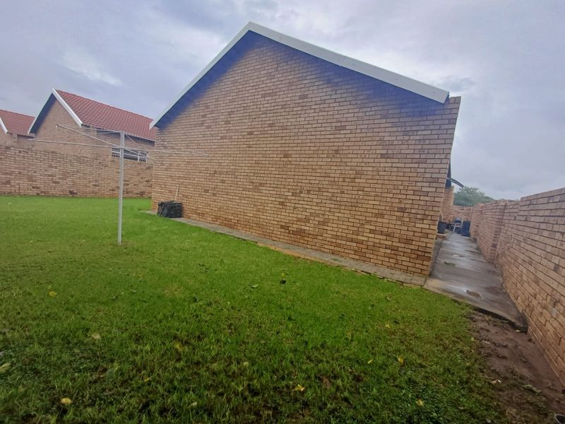 A view of the side and rear exterior of the townhouse, featuring face-brick walls, a lawn area, and a paved walkway.