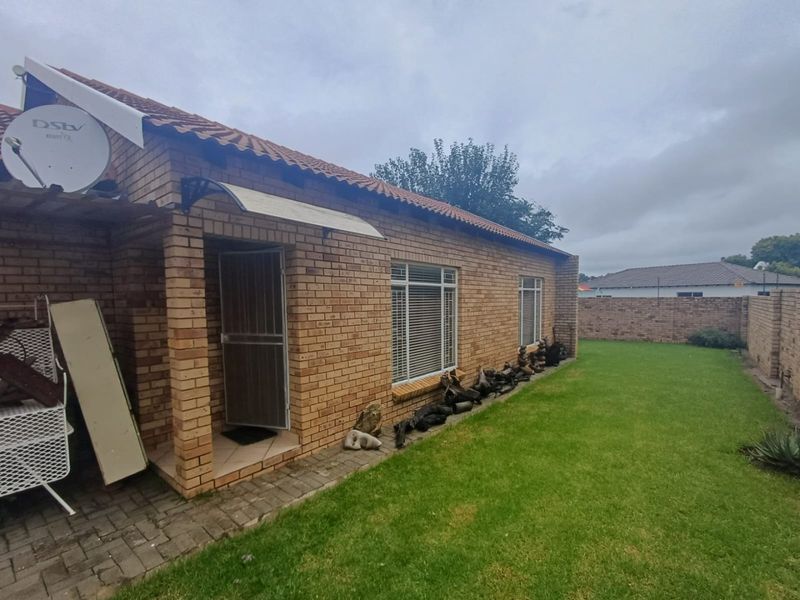 Rear view of the townhouse featuring face-brick exterior, tiled roof, security gate, and a private garden area.