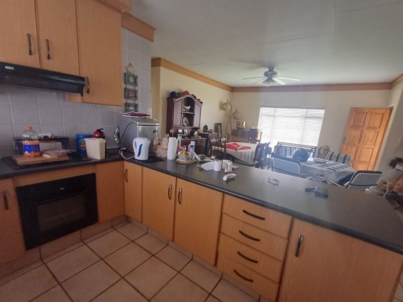 Open plan kitchen and dining area featuring light wood cabinetry, dark countertops, built-in oven, extractor fan, and tiled flooring.