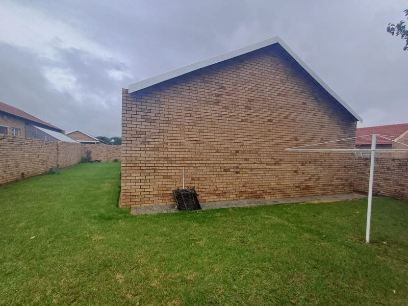 A private rear garden area featuring a brick townhouse exterior wall, lawn space, and perimeter boundary walls.