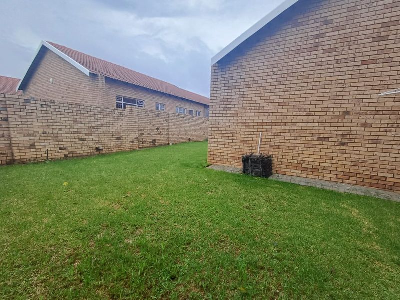 A view of the rear garden area featuring face-brick exterior walls and a grass lawn between townhouse units.