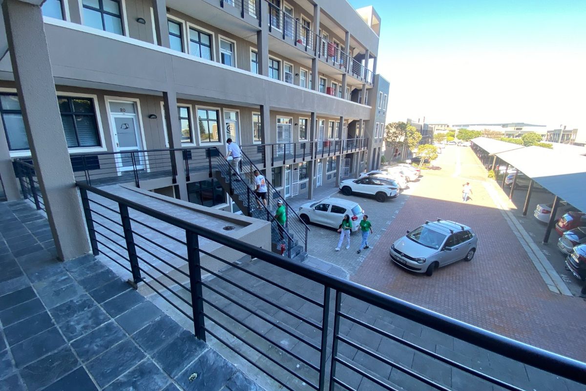 Exterior view of a multi-story commercial office complex featuring paved parking areas, metal staircases, and balcony walkways with black railings.