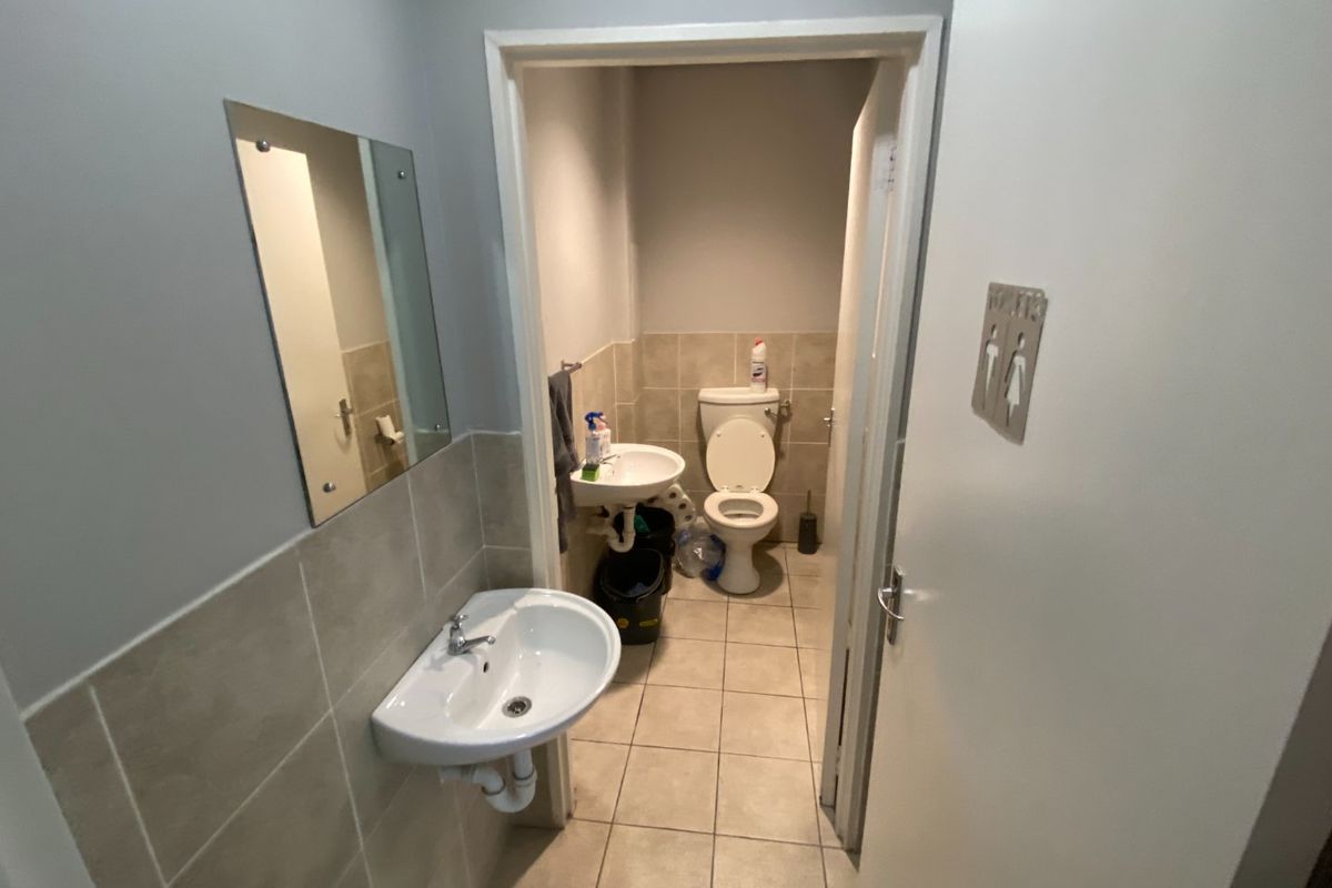 A commercial restroom facility featuring tiled flooring, wall-mounted basins, and a separate toilet cubicle with neutral finishes.