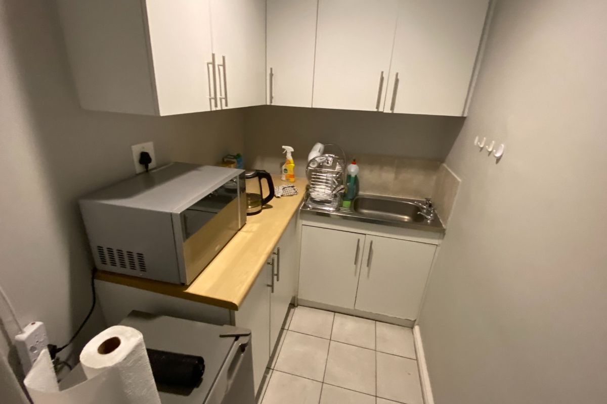 Compact kitchenette featuring white cabinetry, light wood-look countertops, a stainless steel sink, and tiled flooring.