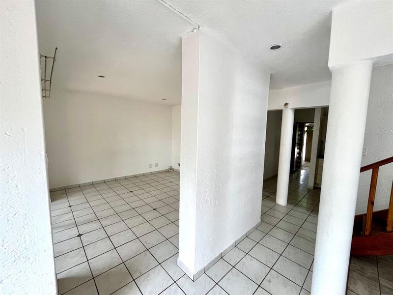 An empty open-plan living area featuring ceramic tile flooring, structural columns, and recessed lighting, offering a blank canvas for interior design.