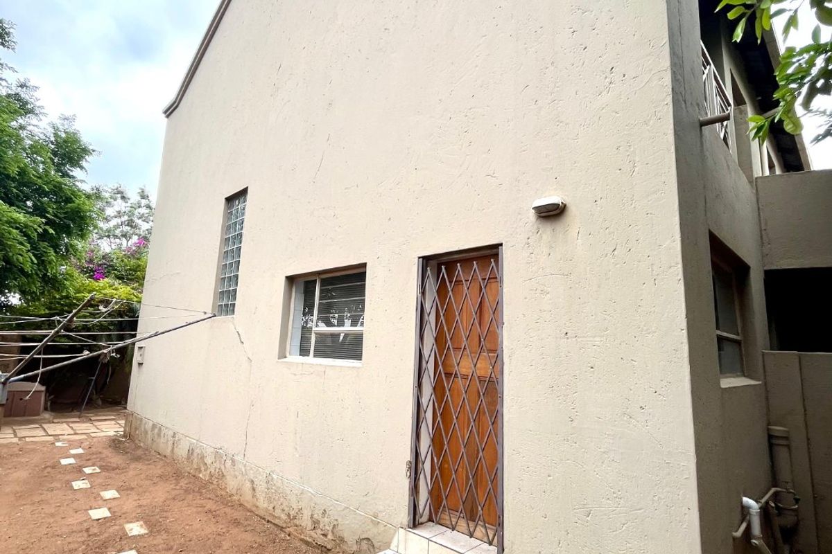 Rear exterior view of the townhouse featuring a security gate, tiled step, and glass block window with visible plaster cracking on the exterior wall.