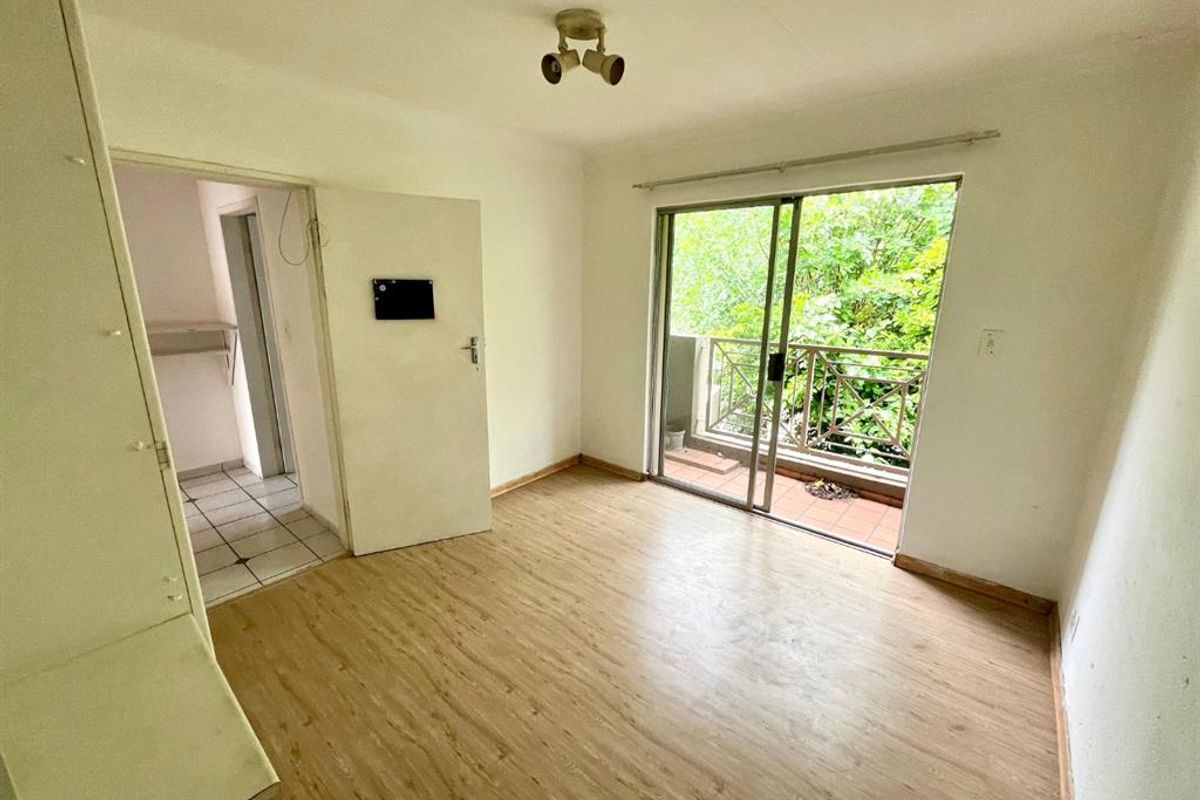 An empty bedroom featuring laminate flooring, a built-in cupboard, and sliding glass doors that open onto a private balcony.