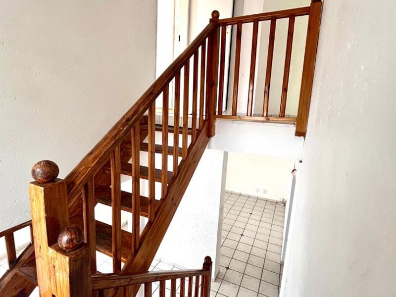 A vacant hallway featuring a traditional wooden staircase with balustrades and tiled flooring, leading to an adjacent room.