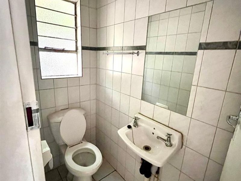 A compact, dated bathroom featuring tiled walls and floors, a wall-mounted basin, and a standard toilet.