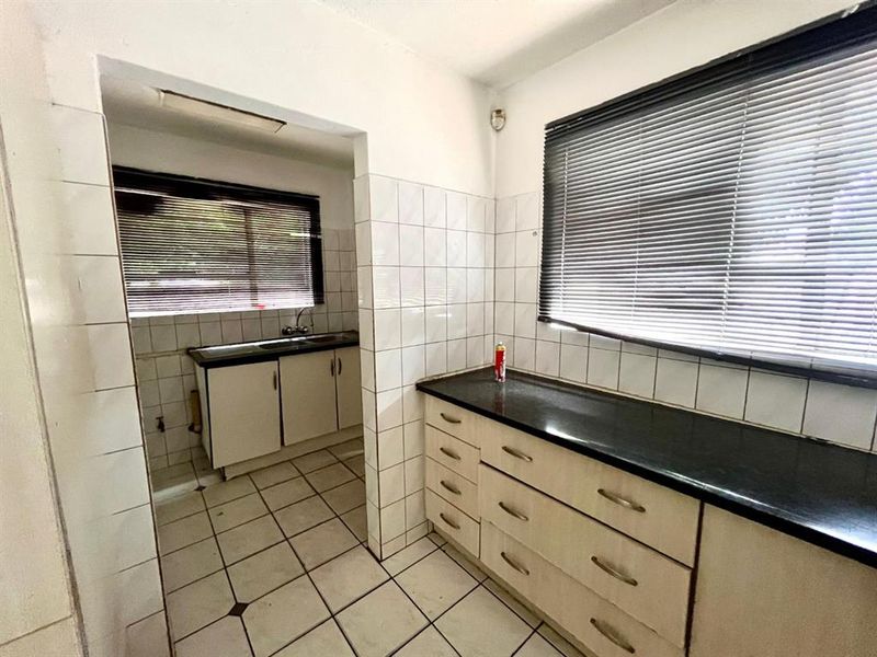 A functional scullery area featuring tiled flooring, ample cabinetry, stone countertops, and a stainless steel sink, offering a practical secondary prep space.