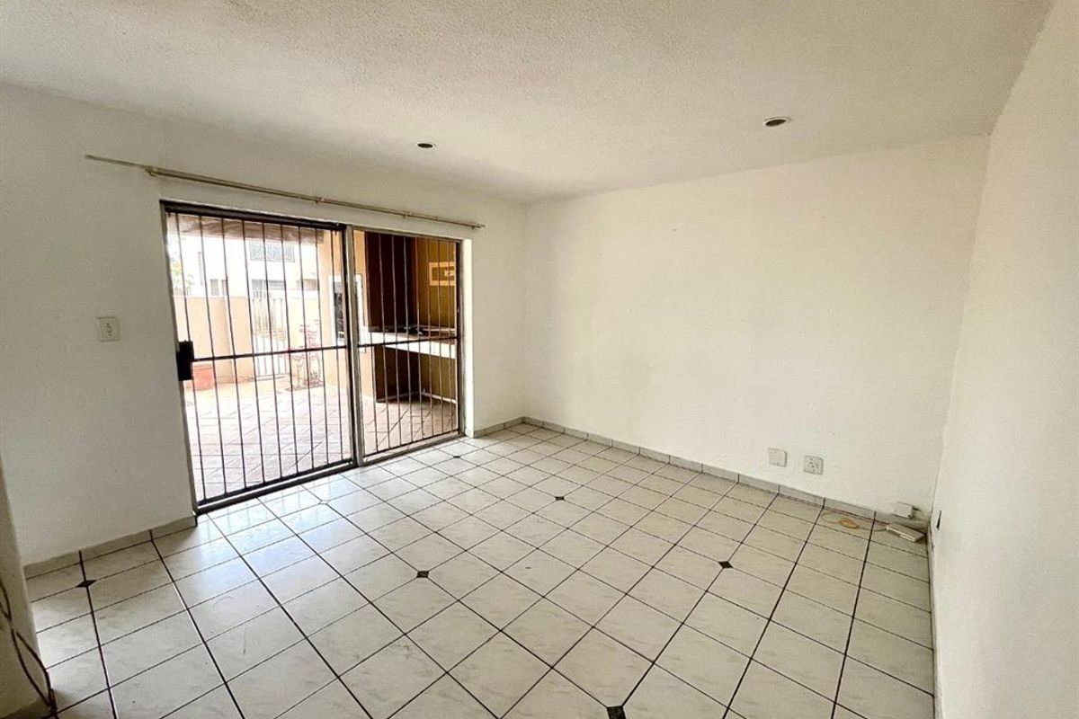 An empty living room featuring tiled flooring and a sliding glass door with security bars, providing direct access to the outdoor patio area.