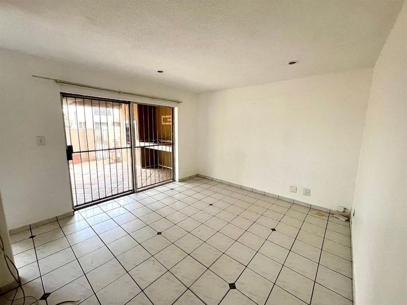 An empty living room featuring tiled flooring and a sliding glass door with security bars, providing direct access to the outdoor patio area.