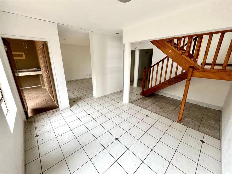 An open-plan living area featuring tiled flooring, a wooden staircase, and structural columns, offering a blank canvas for interior design.